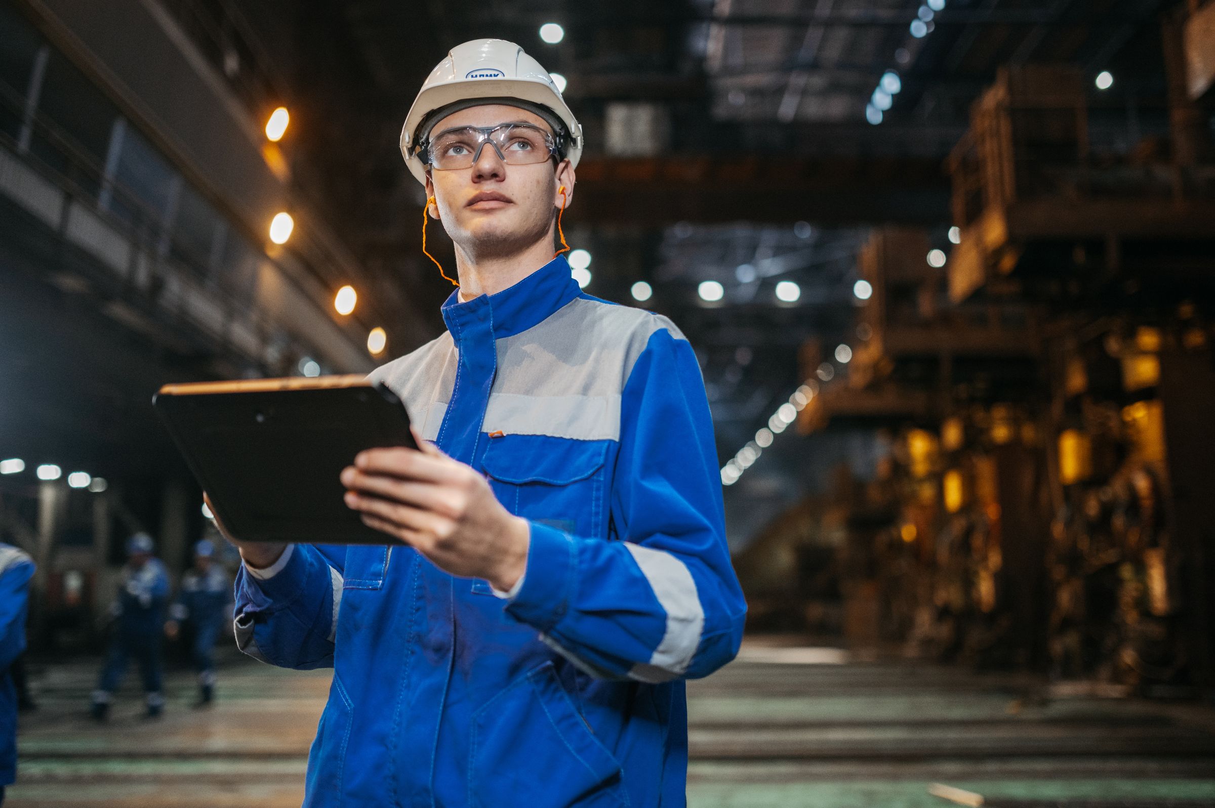 An engineer in protective equipment using a tablet on an industrial site